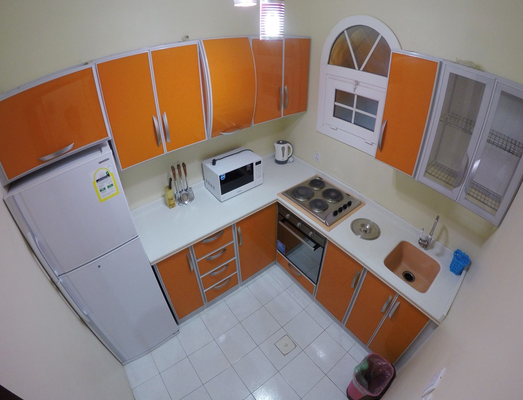 Une cuisine de taille réduite avec des meubles de couleur orange, un réfrigérateur blanc, un four à micro-ondes, une cuisinière et un évier.