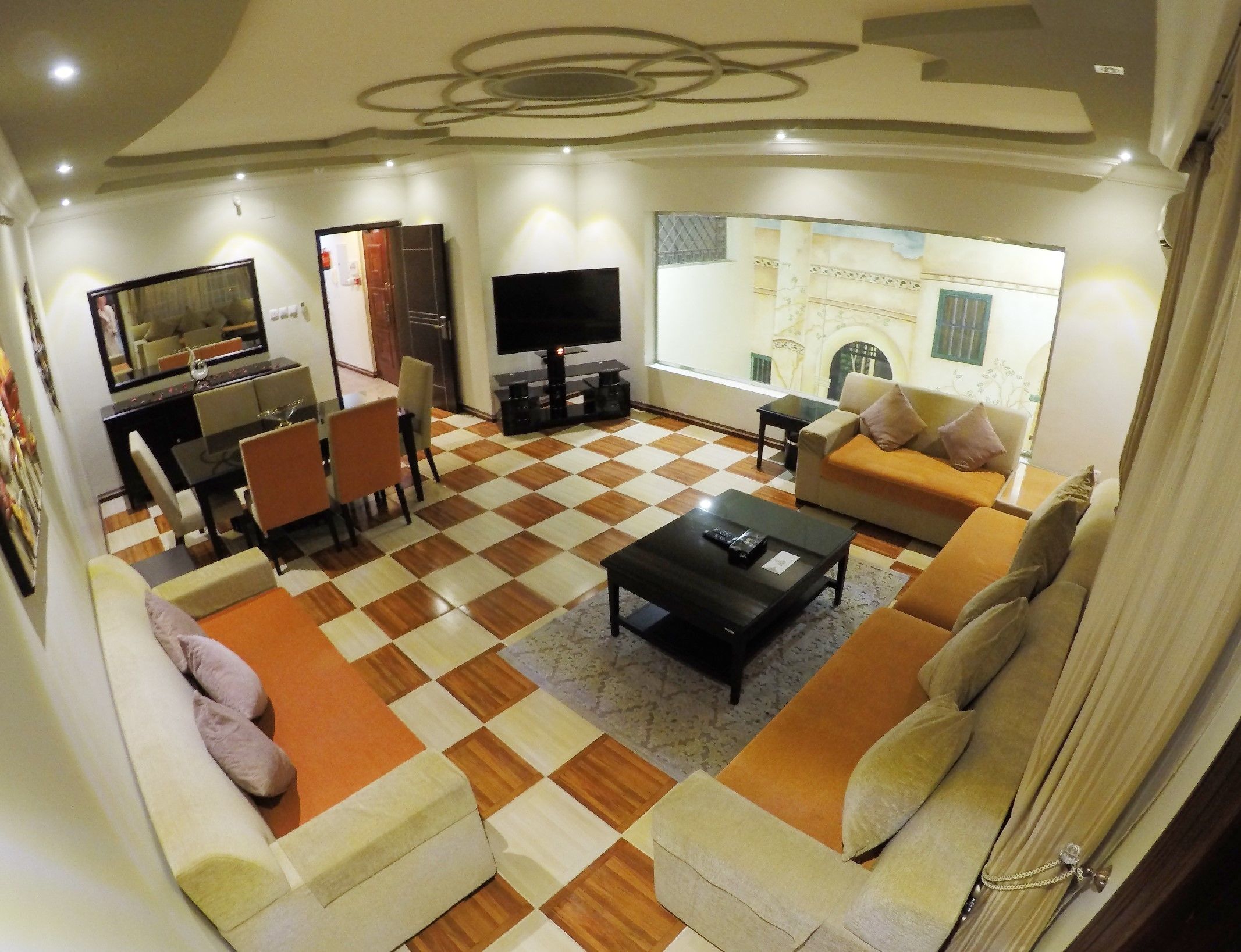 Una sala de estar con piso a cuadros, un sofá, una mesa de centro, un televisor y un comedor con sillas y una mesa.