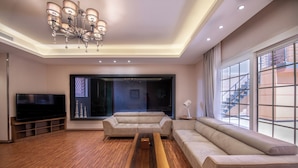 Un salon moderne avec un grand téléviseur à écran plat, une table basse en bois et deux canapés beige.