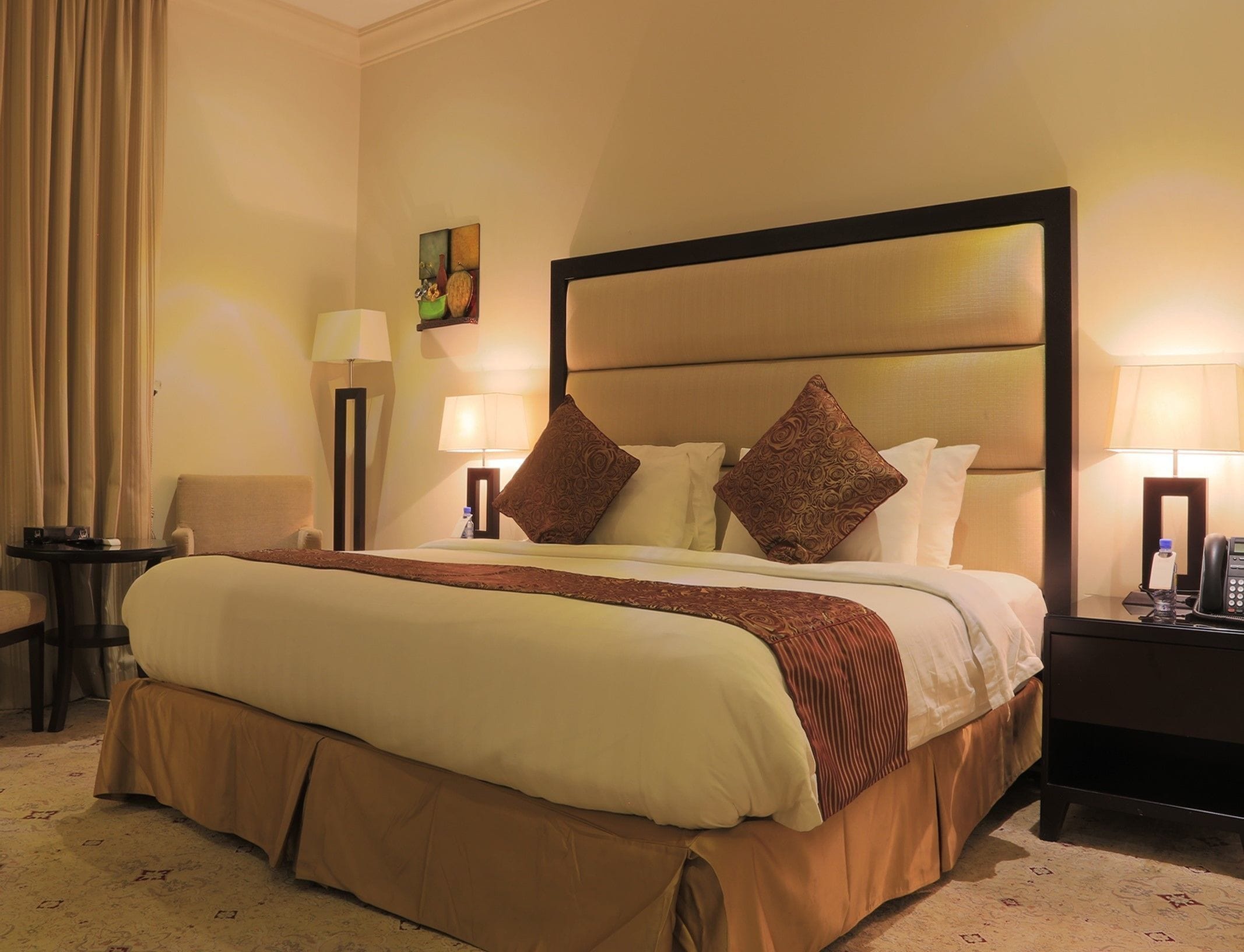 Une chambre d’hôtel avec un grand lit, deux tables de chevet, une chaise, une lampe et un tableau au mur.