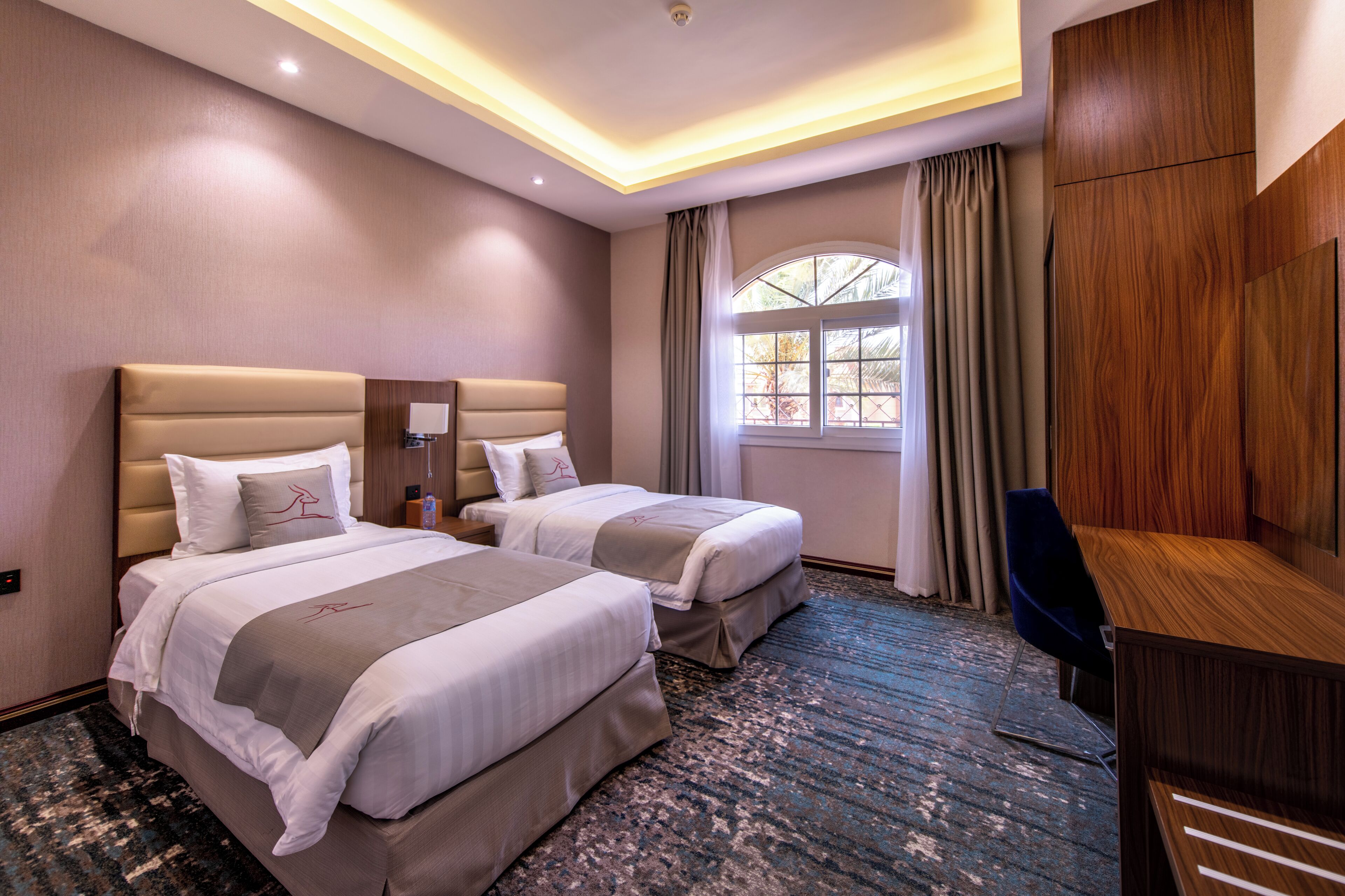 Une chambre d’hôtel avec deux lits, un bureau et une grande fenêtre avec des rideaux.