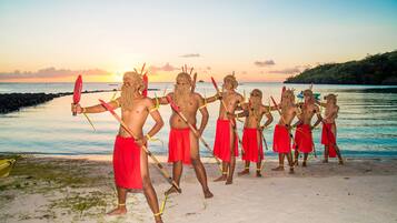 A group of people in traditional attire standing on a beach with a sunset in the background.