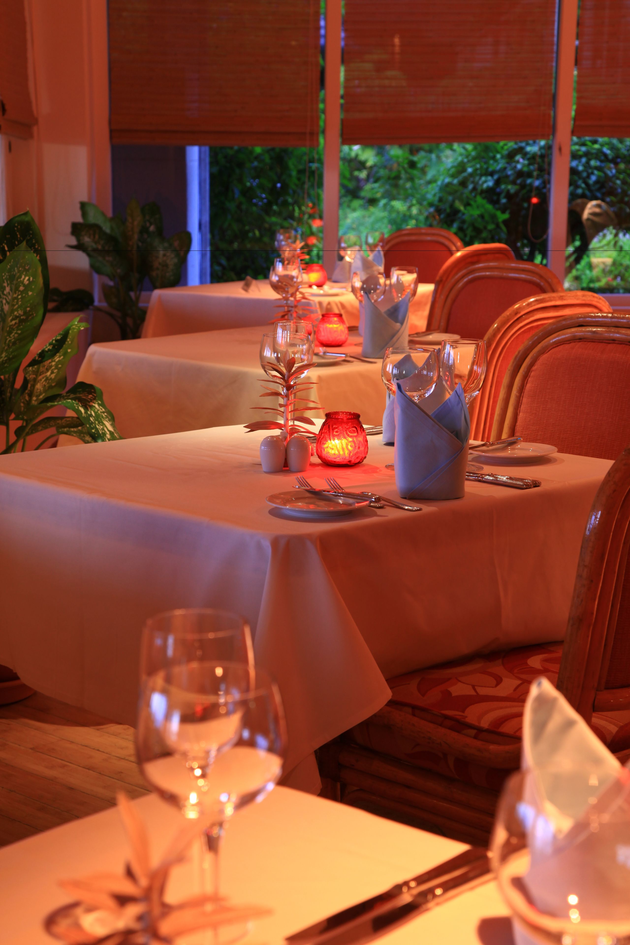 Comedor con mesas dispuestas para una comida, con un centro de mesa con velas y vistas al exterior con follaje.