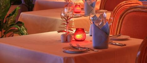 Comedor con mesas dispuestas para una comida, con un centro de mesa con velas y vistas al exterior con follaje.