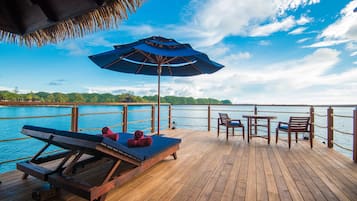 A wooden deck with a lounge chair and a table with chairs, overlooking a body of water.