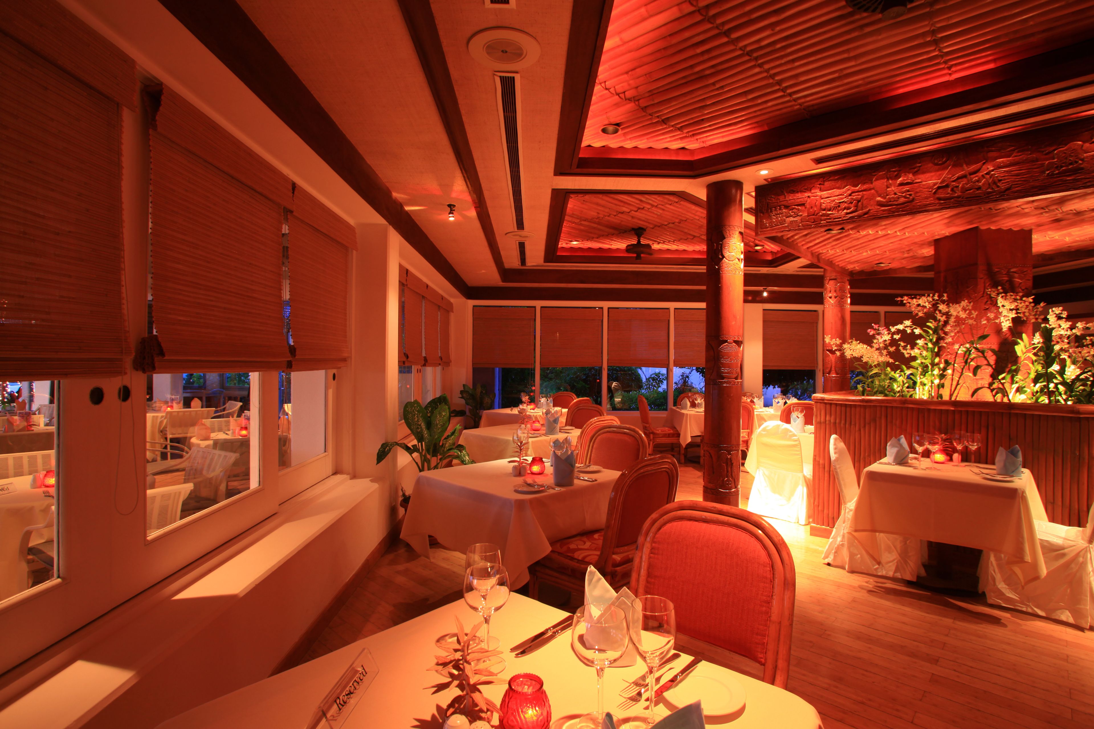A restaurant with multiple tables set for dining, large windows, and a warm interior ambiance.