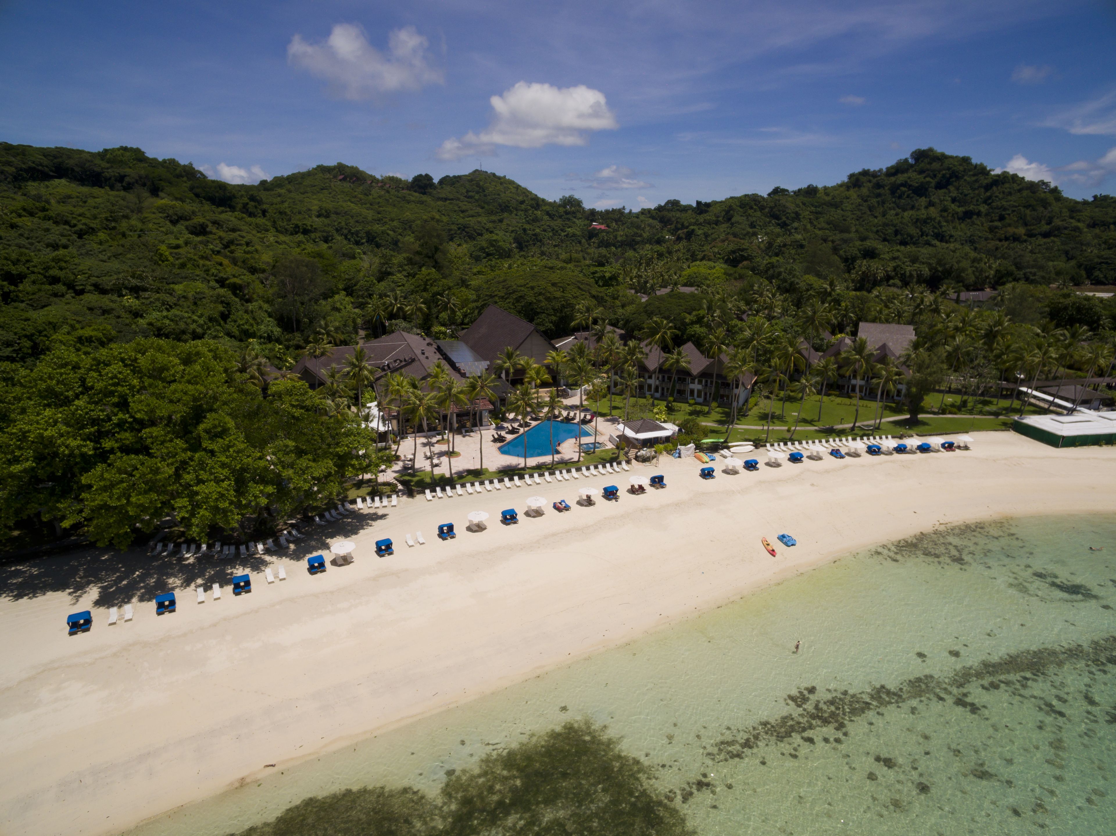 Vista aérea de un complejo turístico con piscina, sombrillas de playa y villas.
