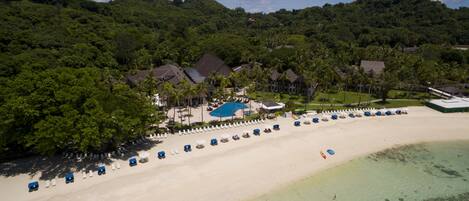 Vista aérea de un complejo turístico con piscina, sombrillas de playa y villas.