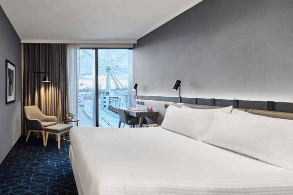 Habitación de hotel con una cama grande, un escritorio, una silla y vistas a una noria.