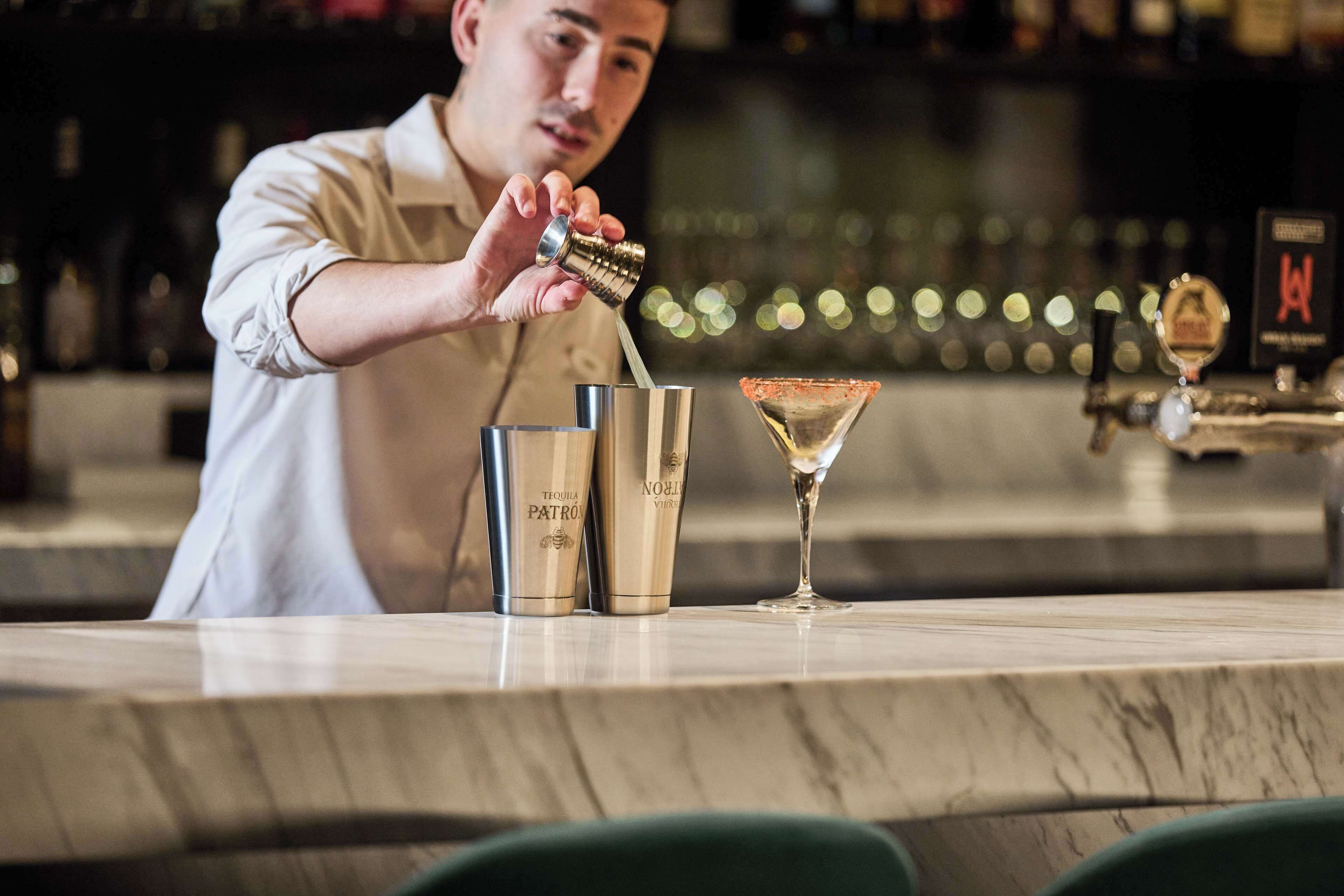 A bartender pouring a drink into a martini glass.