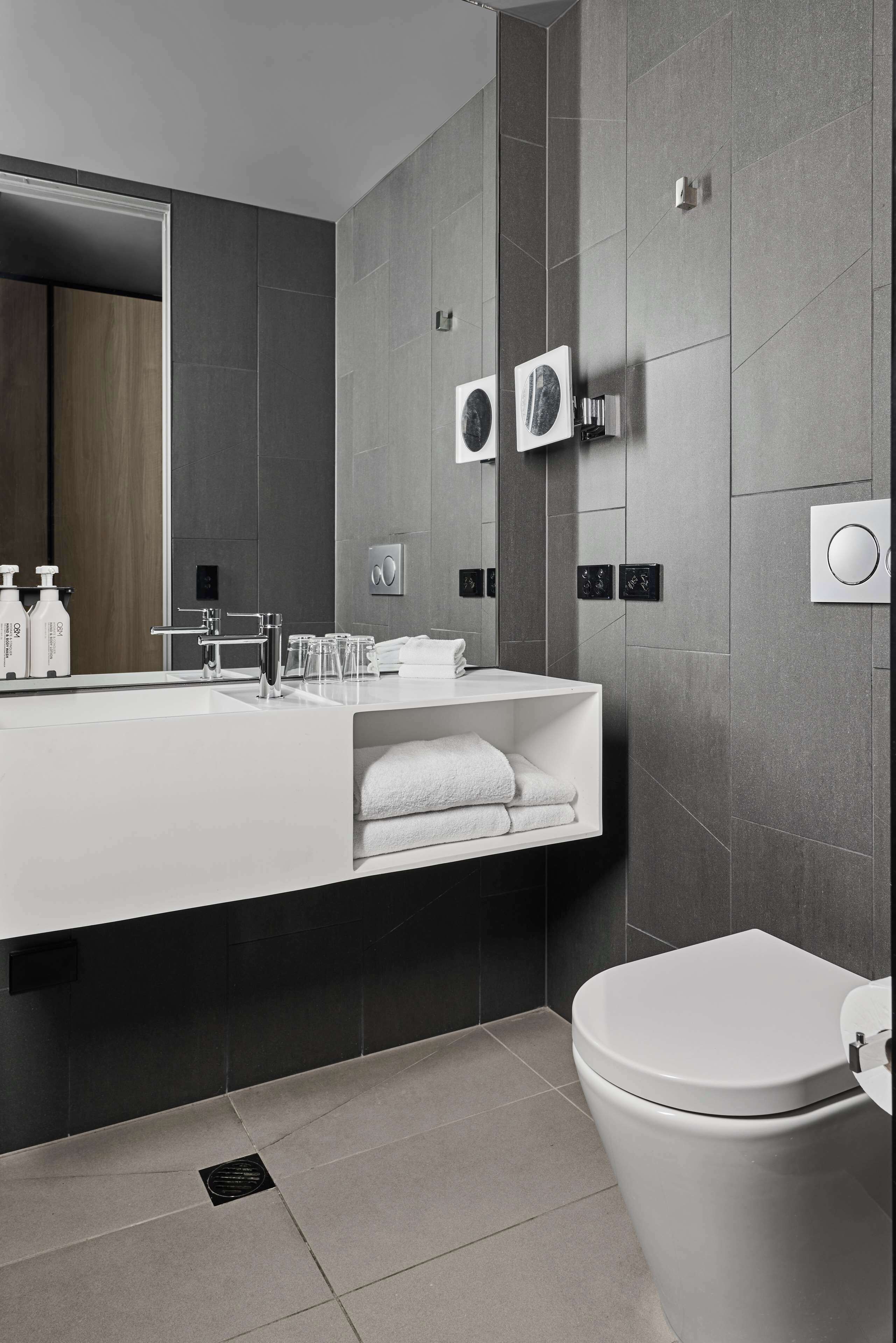 A modern bathroom with a large mirror, white sink, and a toilet.