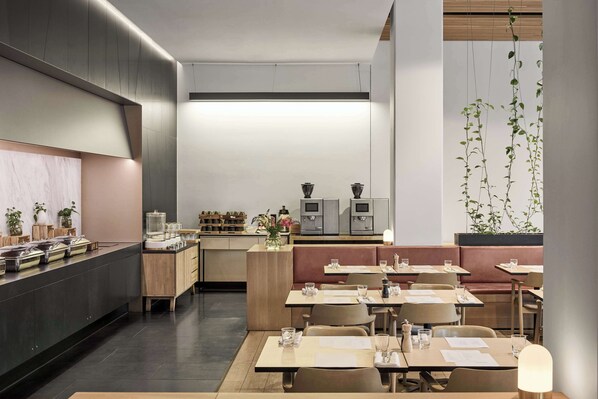 Un restaurante moderno con una barra larga, mesas de madera y cabinas. Hay plantas y una máquina de café al fondo.