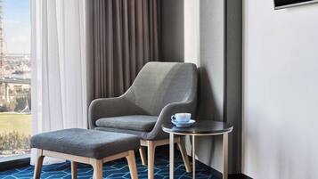 Una habitación de hotel moderna con un sillón tapizado gris, un reposapiés a juego y una pequeña mesa redonda con una taza.