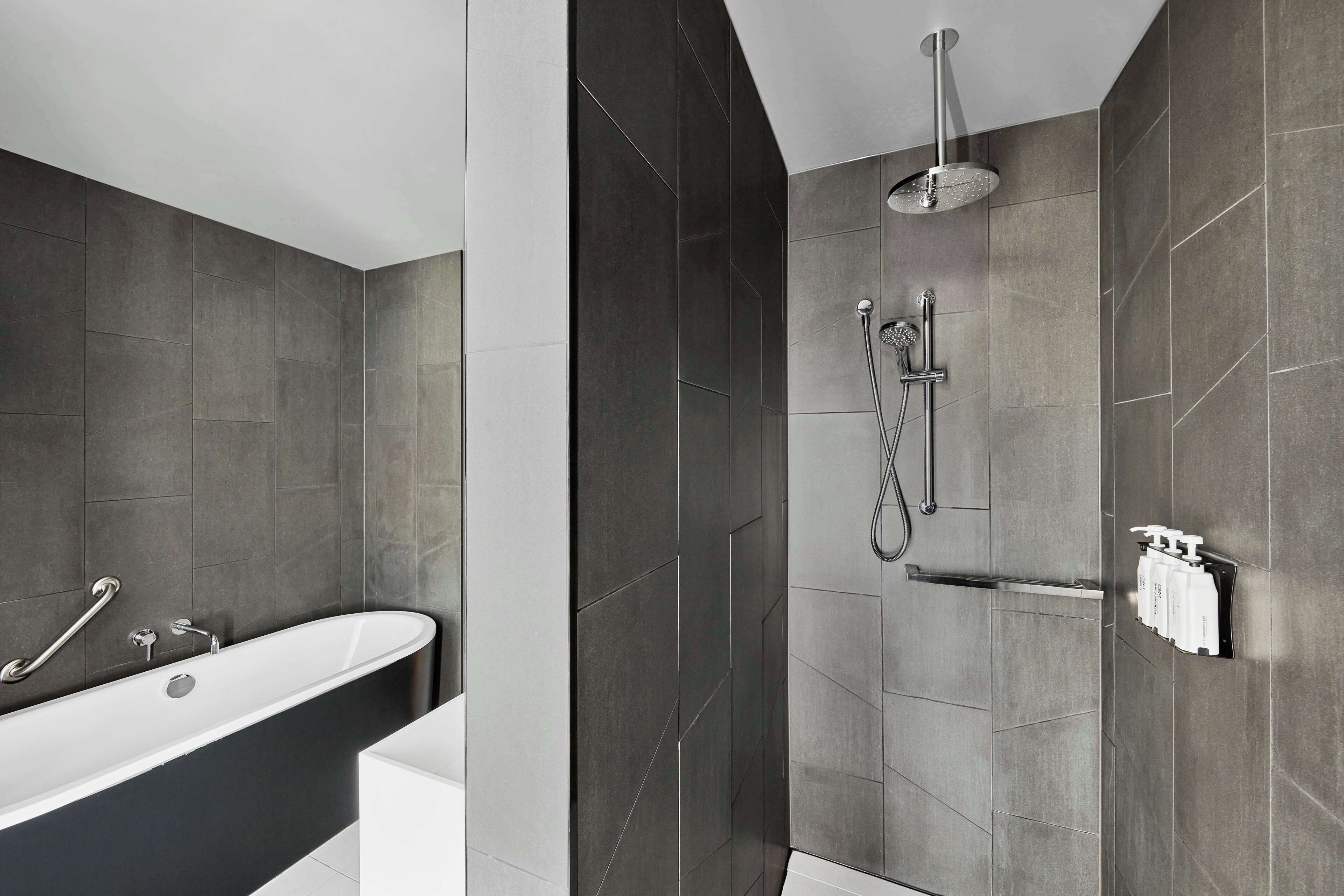 Un baño moderno con una bañera independiente, ducha con cabezal de lluvia y un perchero con artículos de aseo.