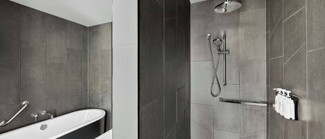Un baño moderno con una bañera independiente, ducha con cabezal de lluvia y un perchero con artículos de aseo.