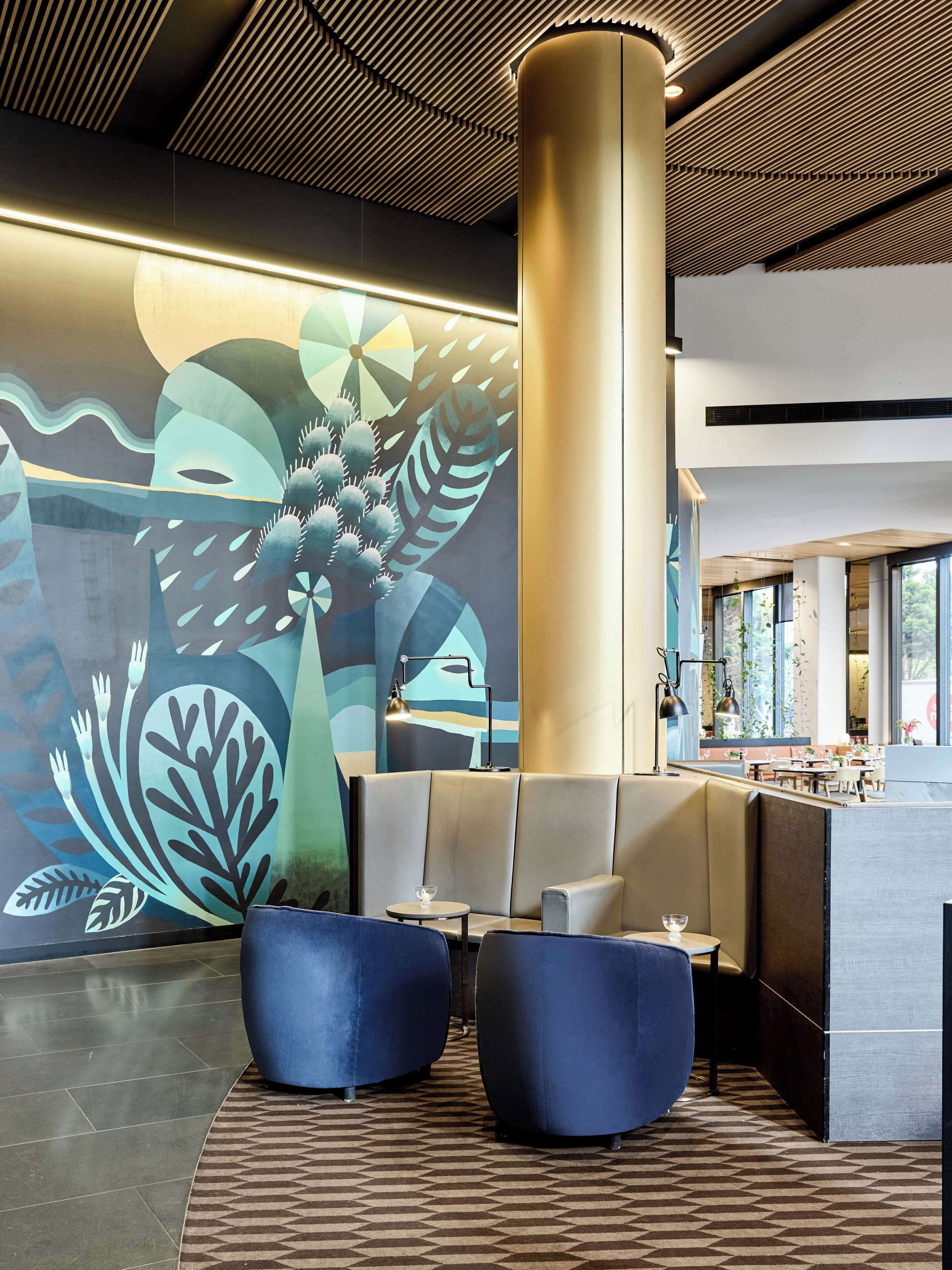 A modern lobby with a large abstract mural, a central pillar, and seating areas.