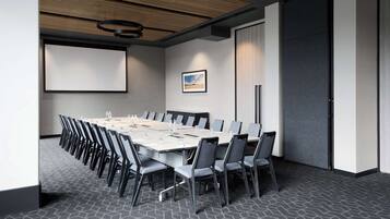Ein Konferenzraum mit langem Tisch, Stühlen, einer Projektionsleinwand und einem gerahmten Bild an der Wand.