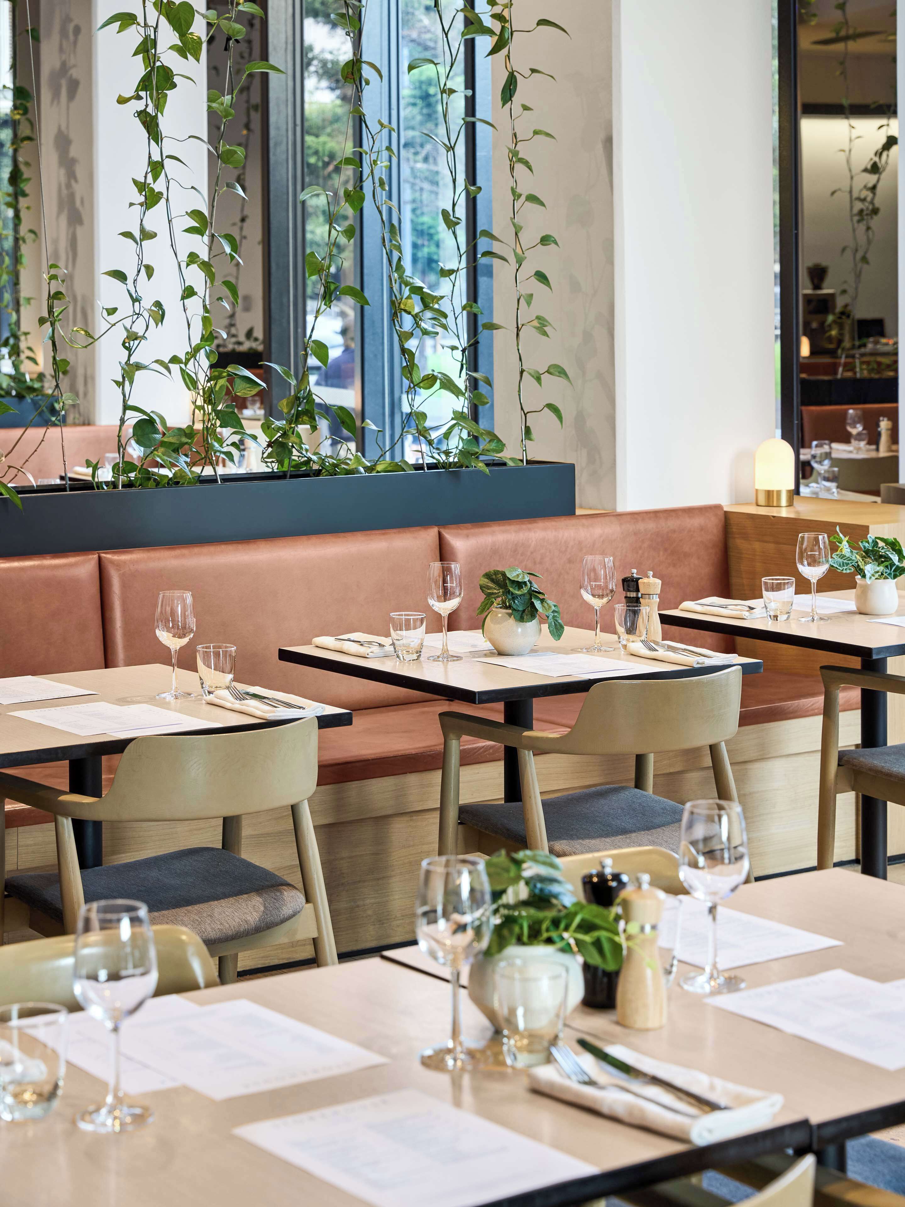 Ein Restaurant mit Sitzecken und Tischen, an jedem Tisch Weingläser, Speisekarten und Besteck.