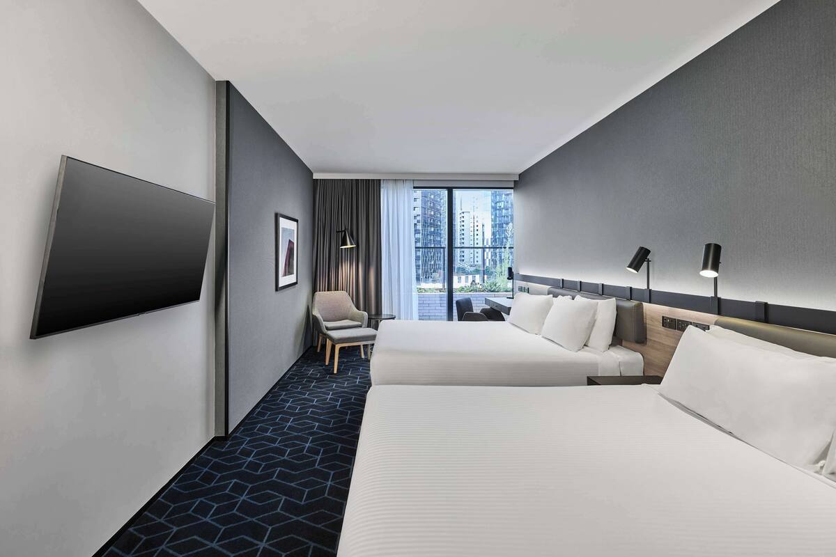 Ein Hotelzimmer mit zwei Betten, einem Flachbildfernseher, einem Schreibtisch und einem Stuhl.