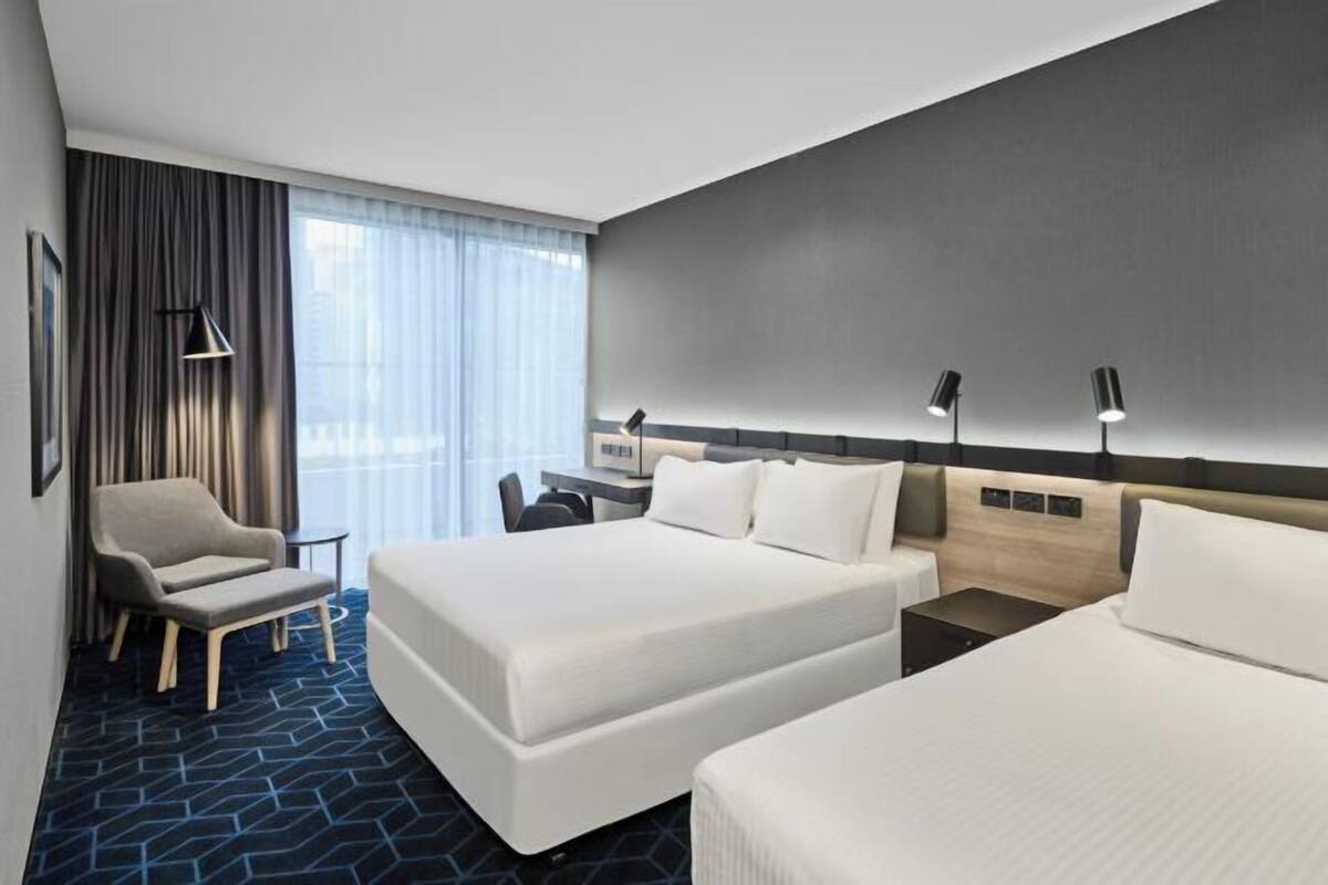 Ein Hotelzimmer mit zwei Betten, einem Schreibtisch, einem Stuhl und einem großen Fenster mit Vorhängen.