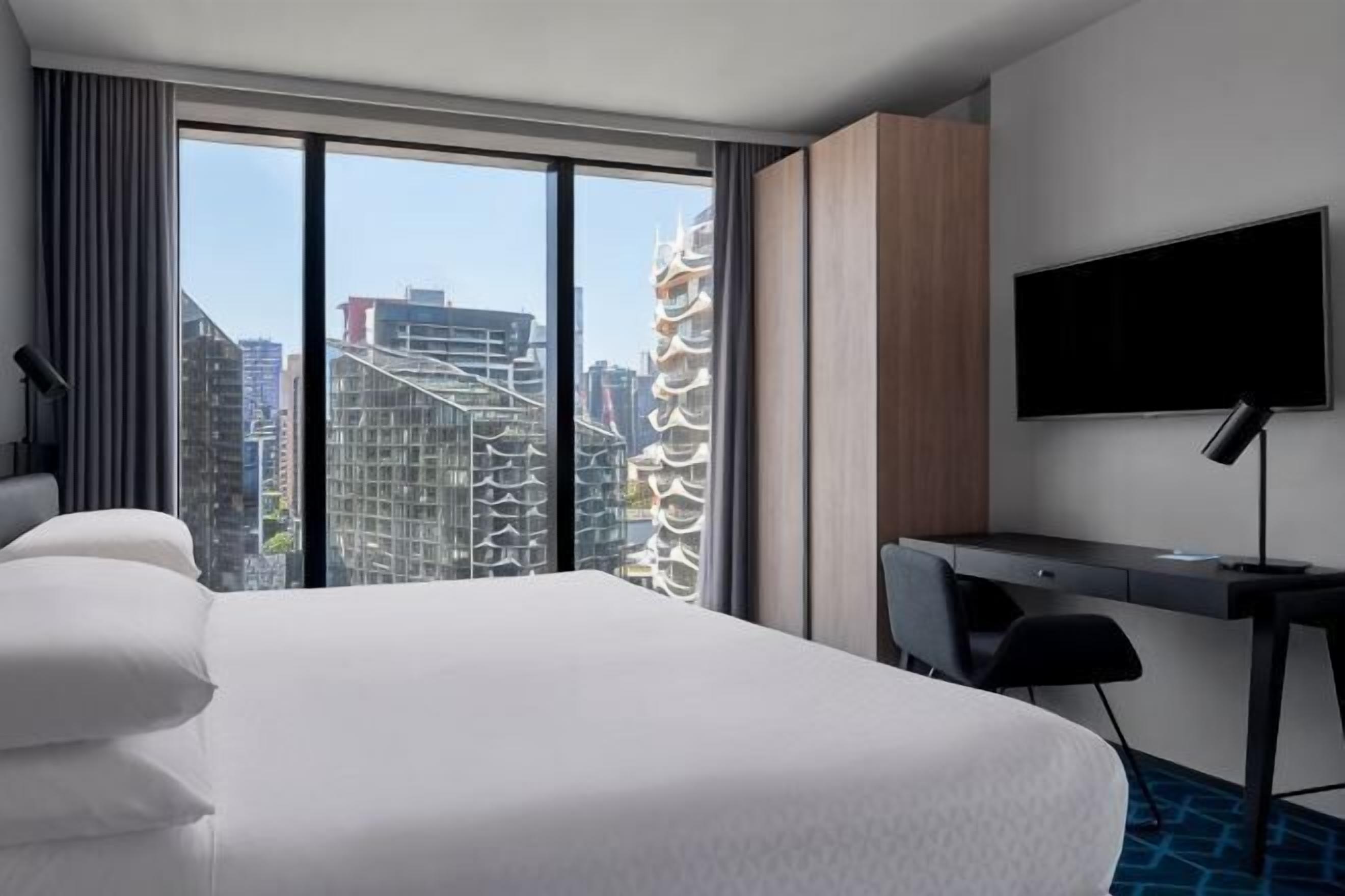 A hotel room with a large bed, a desk, a TV, and a view of the cityscape.