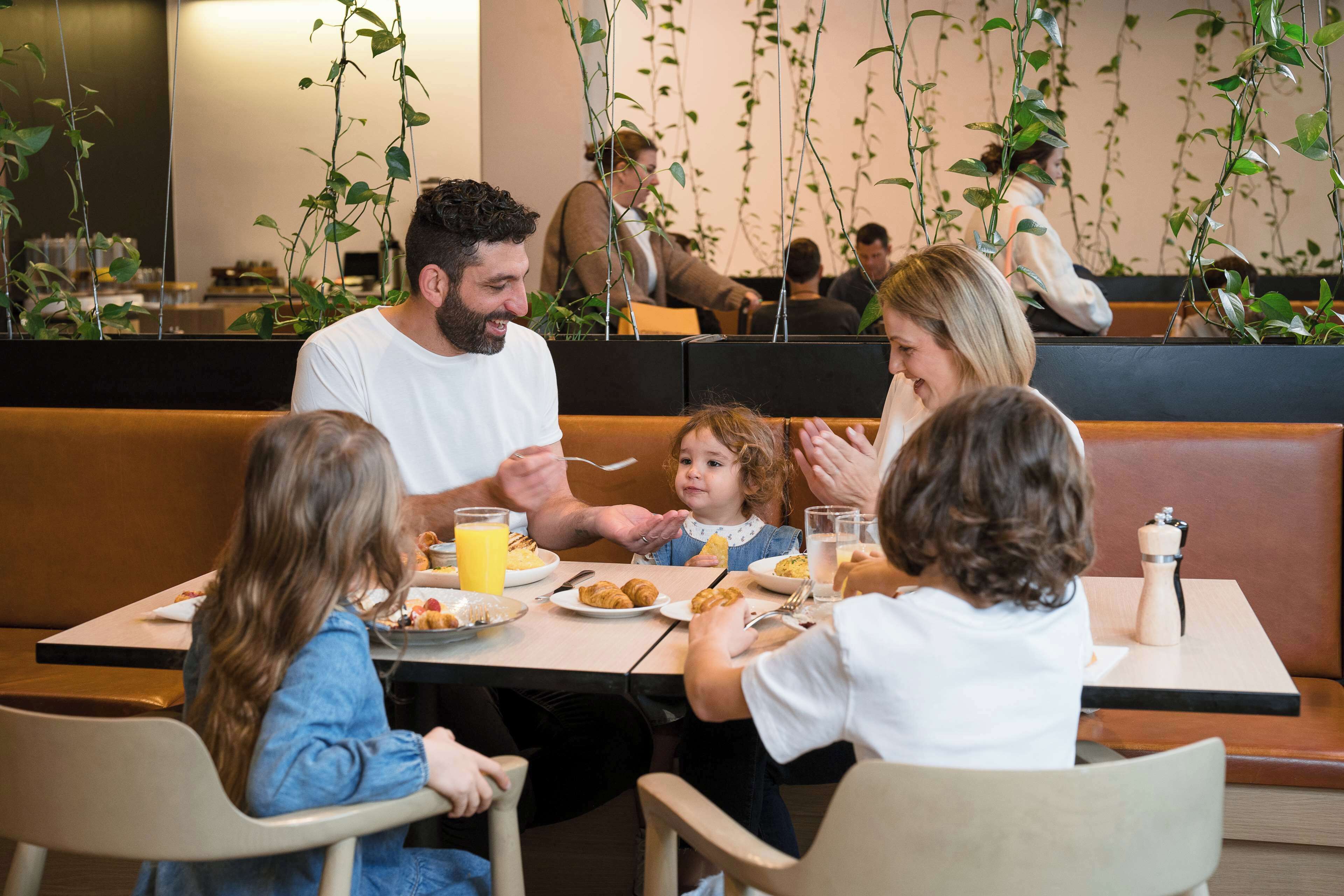 A family dining at a restaurant with a booth seating arrangement, a casual atmosphere, and hanging plants in the background.
