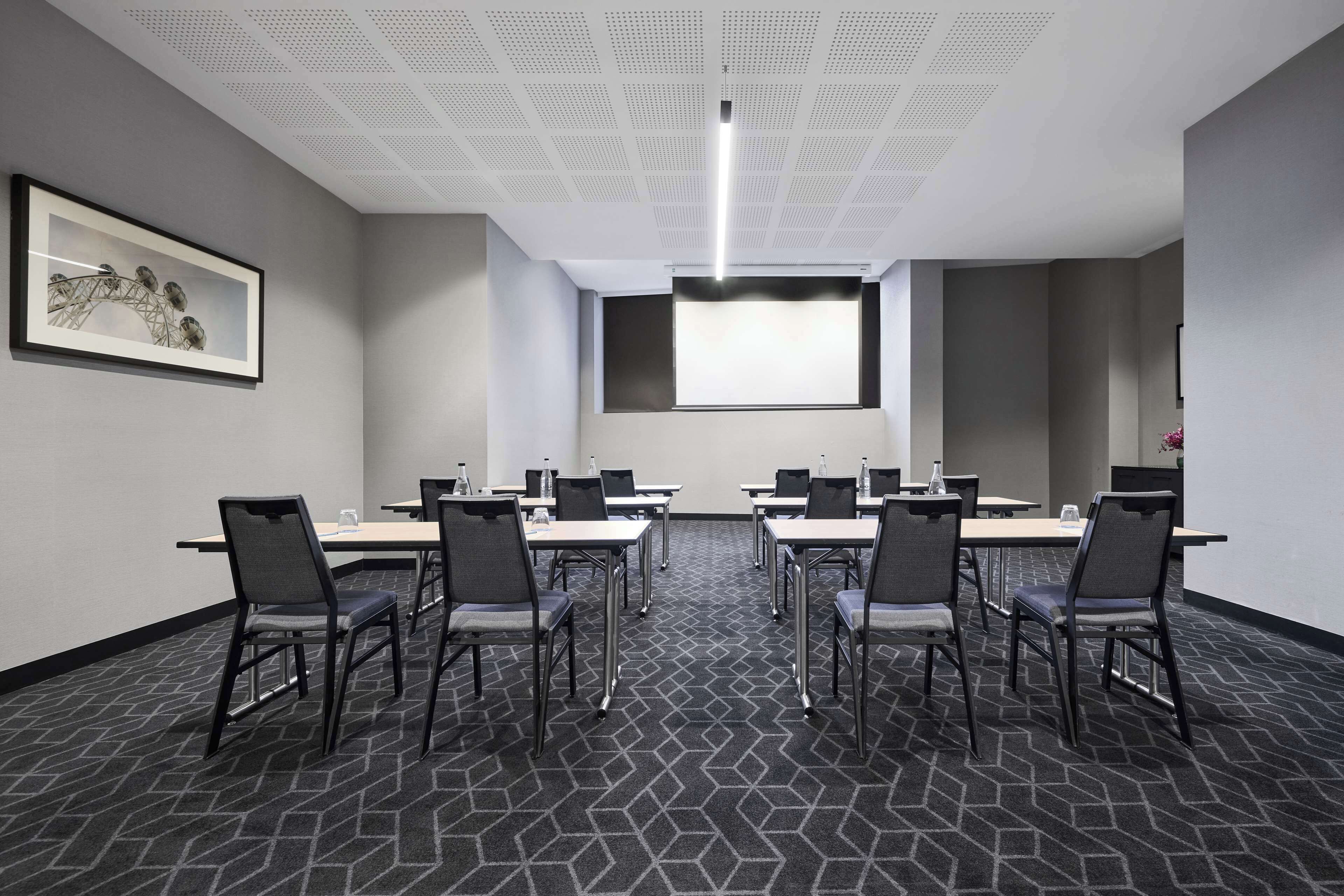 Un salón de conferencias con una pantalla grande, varias mesas y sillas.