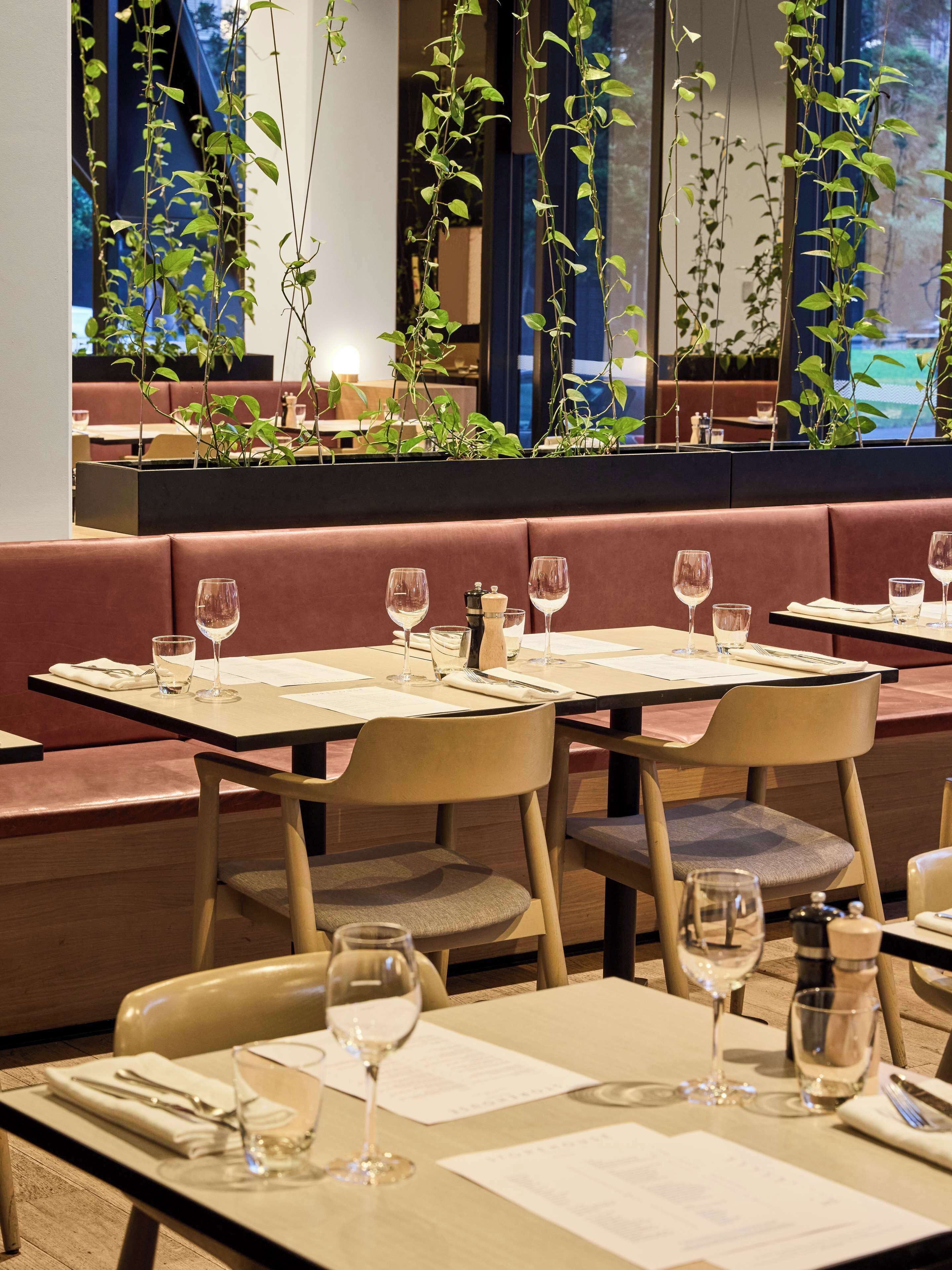 A restaurant with tables set for dining, featuring a view of indoor plants and a modern interior design.