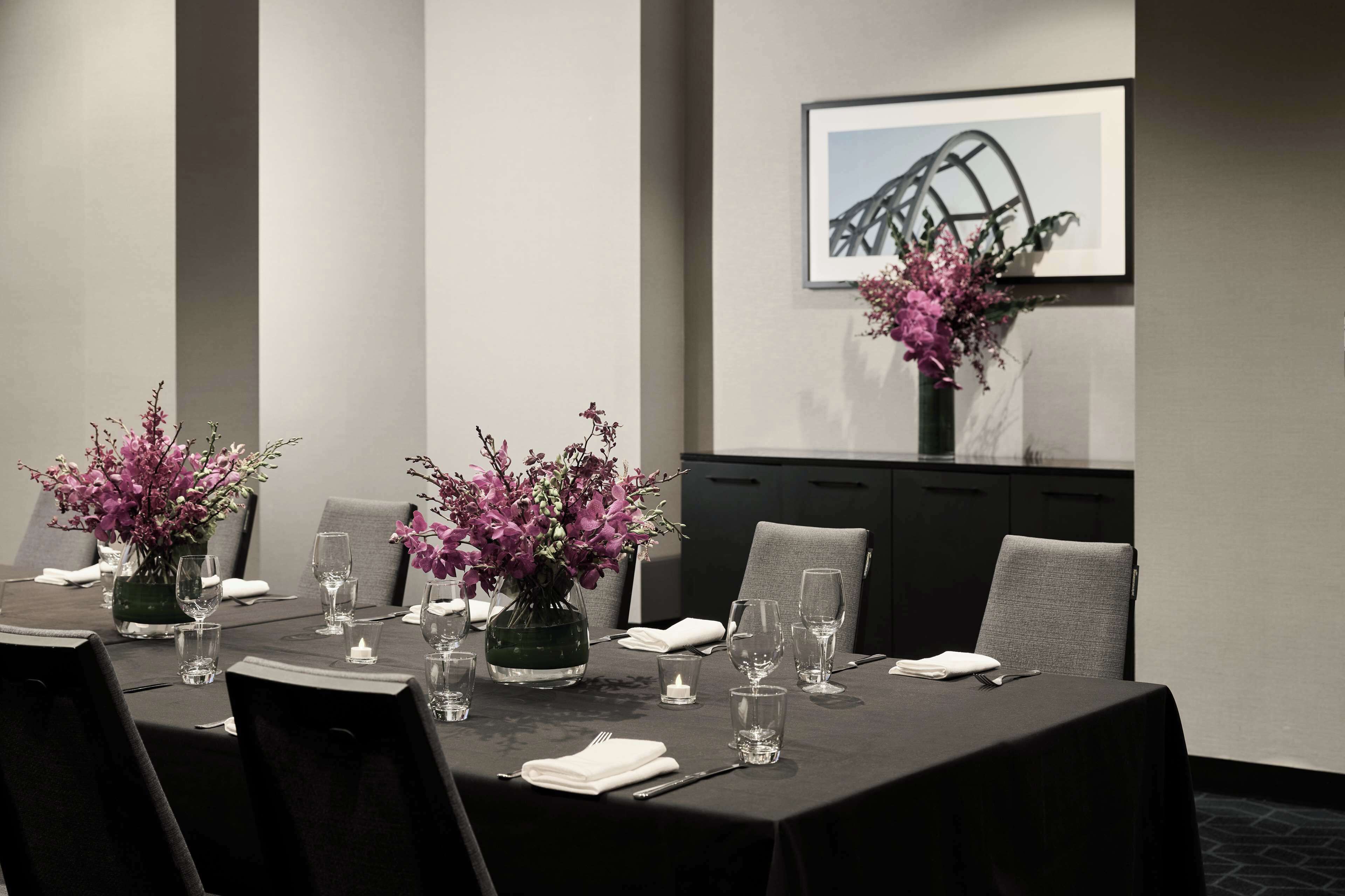 A conference room with a long table set for a meeting, equipped with chairs, a vase of flowers, and glassware.