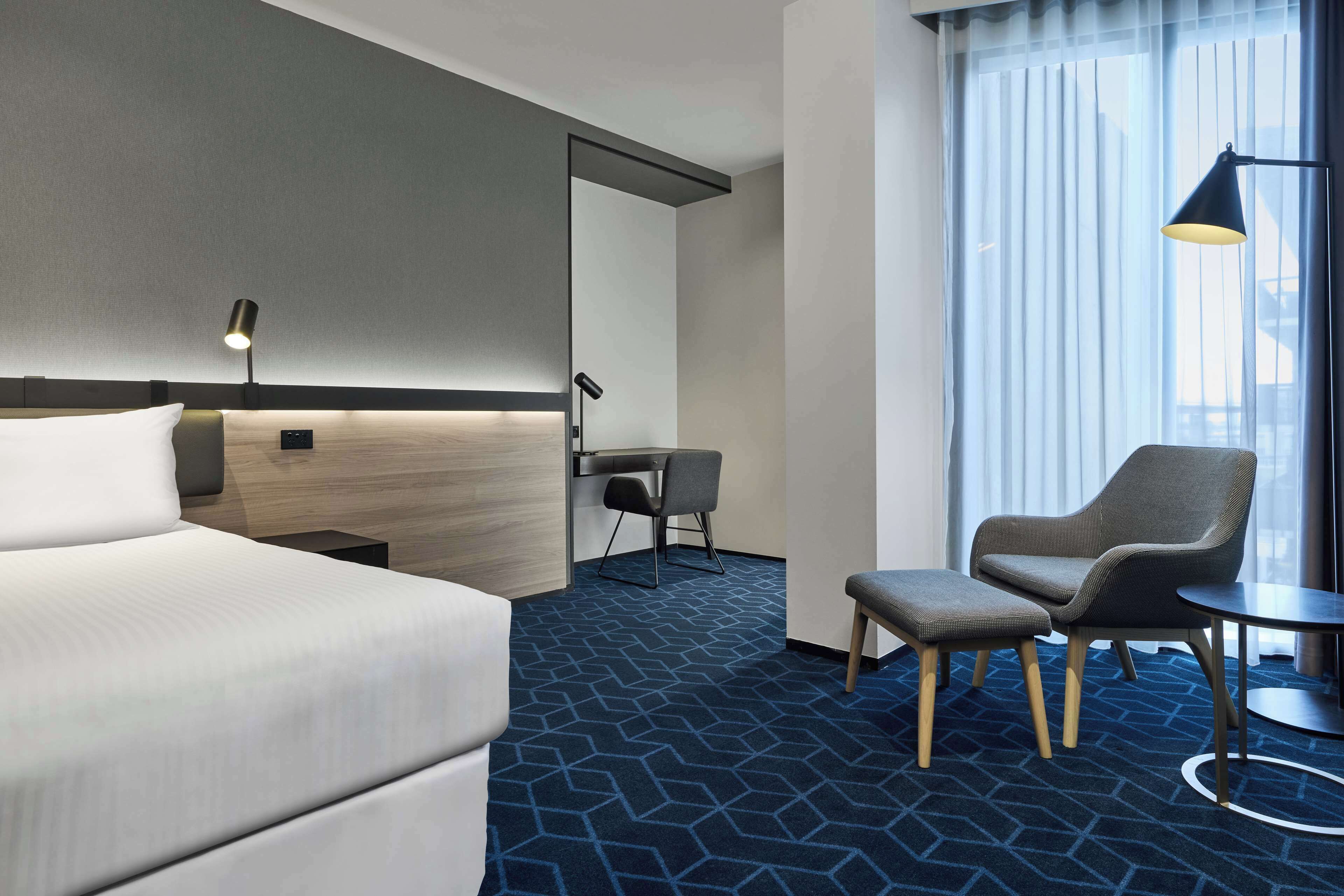 Una habitación de hotel con una cama grande, un escritorio, dos sillas y una mesita.