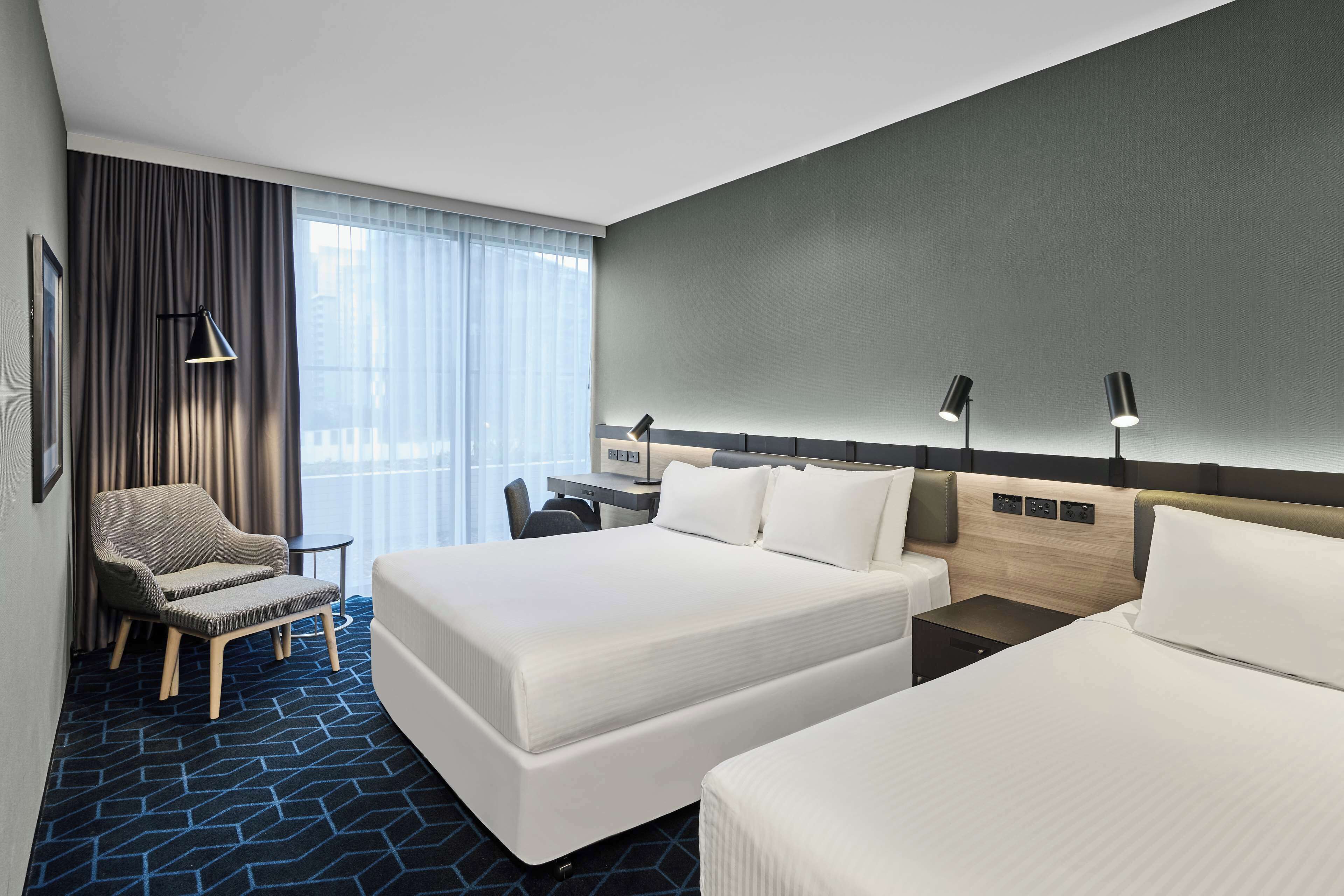 A hotel room with two beds, a desk, a chair, and a large window with curtains.