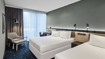 A hotel room with two beds, a desk, a chair, and a large window with curtains.