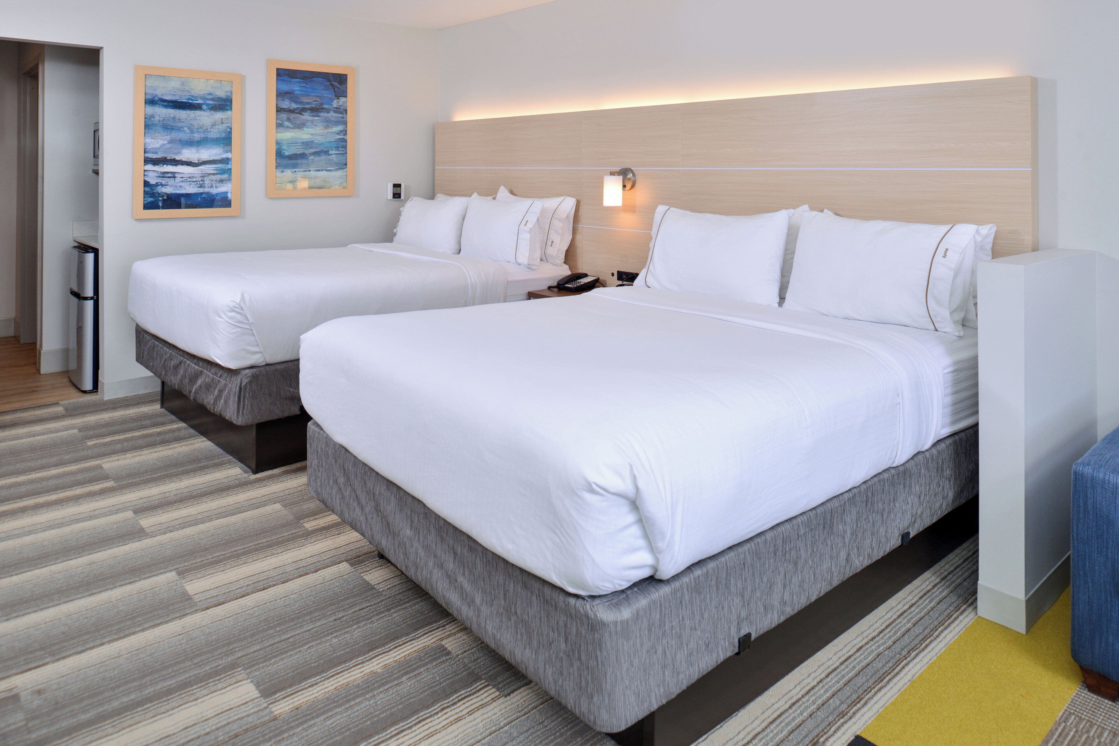 Una habitación de hotel con dos camas, una mesita de noche con lámpara y una obra de arte en la pared.