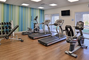 Un gimnasio con cintas de correr, mancuernas y un televisor en la pared.