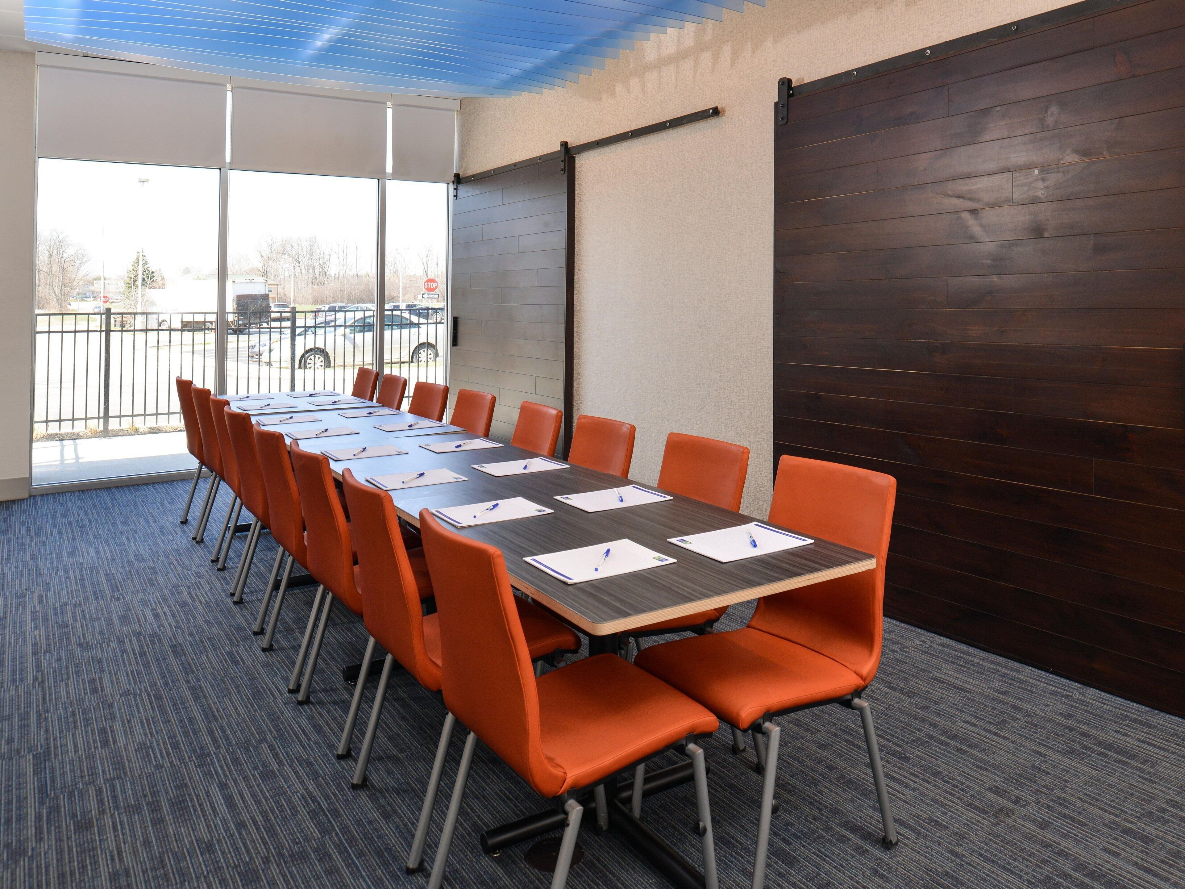 A conference room with a long table, orange chairs, and a view through large windows.