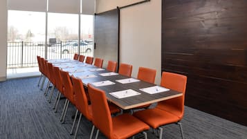 A conference room with a long table, orange chairs, and a view through large windows.