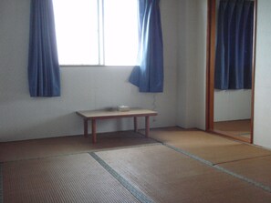A room with tatami flooring, a small wooden table, and a window with blue curtains. - Hoshisunaso (Yoron)