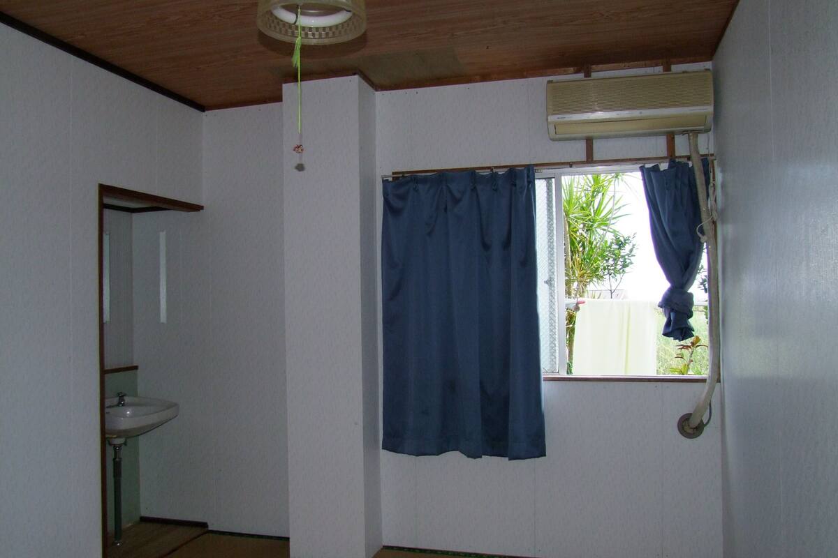 A bathroom with a sink, a window with a curtain, and an air conditioning unit.