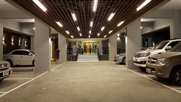 A parking garage with multiple cars parked, a person walking, and a staircase leading to an upper level. - Ploen Place Residence (Pattaya)