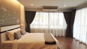 A hotel room with a large bed, a ceiling air conditioner, and sheer curtains on the windows. - Ploen Place Residence (Pattaya)