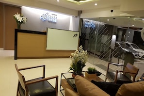 A reception area with a reception desk, seating area, and a view of a parking garage. - Ploen Place Residence (Pattaya)