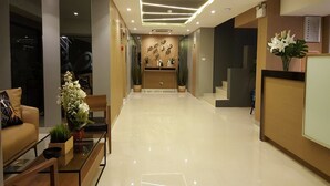 A modern reception area with a clean, polished floor, a reception desk, and a seating area with a sofa and a coffee table. - Ploen Place Residence (Pattaya)