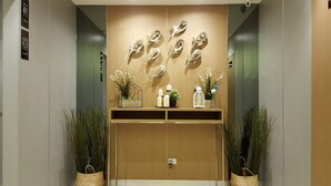 A modern elevator with a wooden finish, two potted plants, and a wall-mounted decorative piece. - Ploen Place Residence (Pattaya)