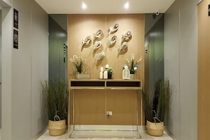 Un ascensor moderno con detalles de madera, dos plantas en macetas y un adorno en la pared.