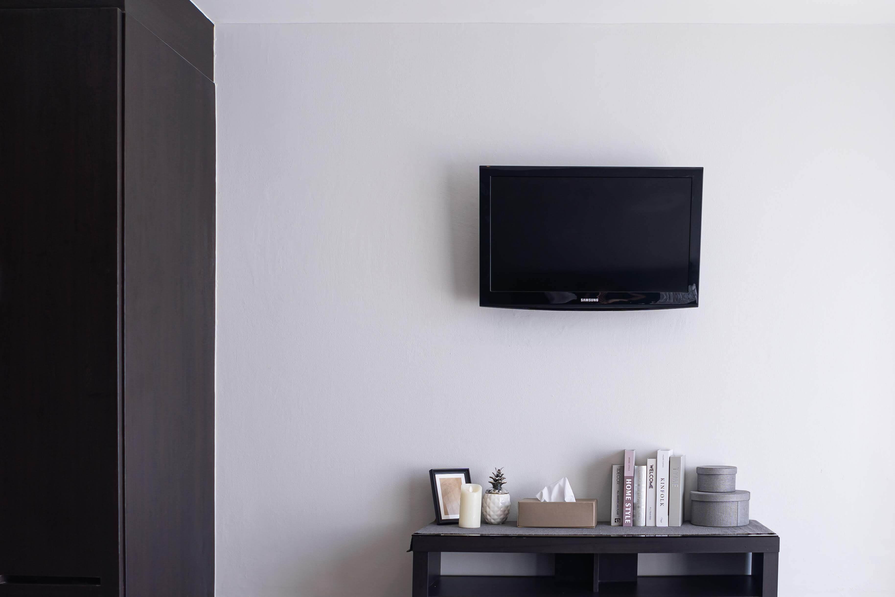 A room with a mounted TV on the wall, a small table with books, a candle, and a tissue box.