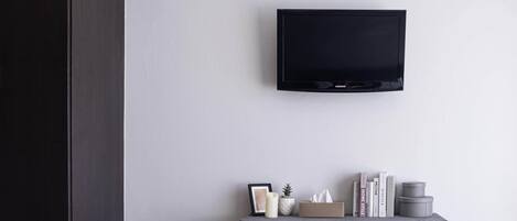 A room with a mounted TV on the wall, a small table with books, a candle, and a tissue box.