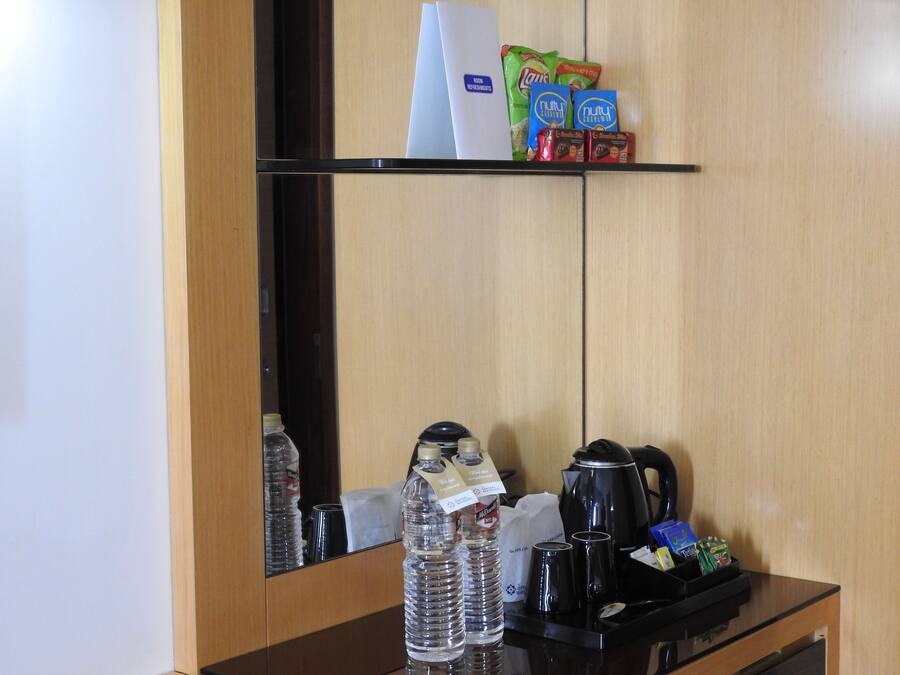 Ein Hotelzimmer mit Holzschrank, einer Ablage für Snacks, einer Kaffeemaschine und abgefülltem Wasser.