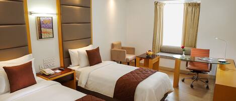 Quarto de hotel com duas camas, uma escrivaninha, uma cadeira e uma janela com cortinas.