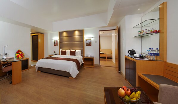 A hotel room with a bed, desk, chair, and a fruit bowl.