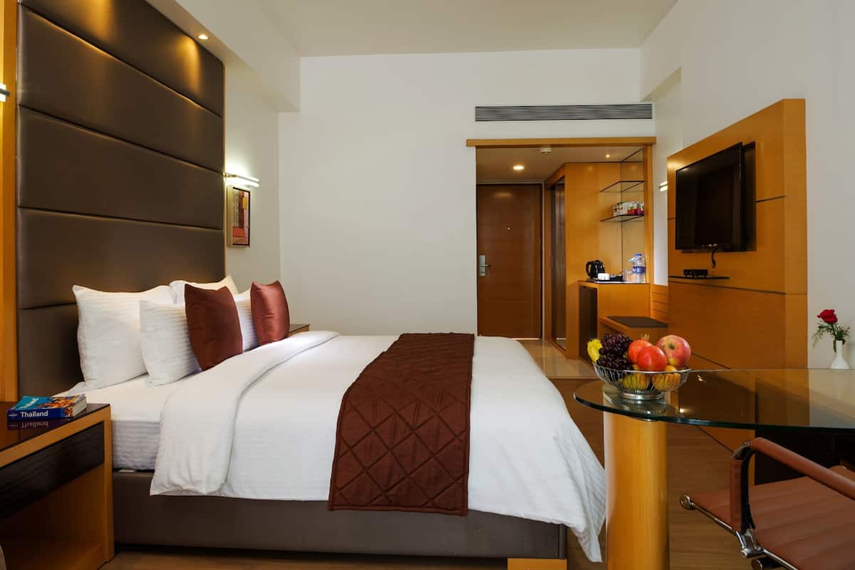 Una habitación de hotel moderna con una cama grande, una mesita de vidrio con fruta, un televisor y un mueble de madera.